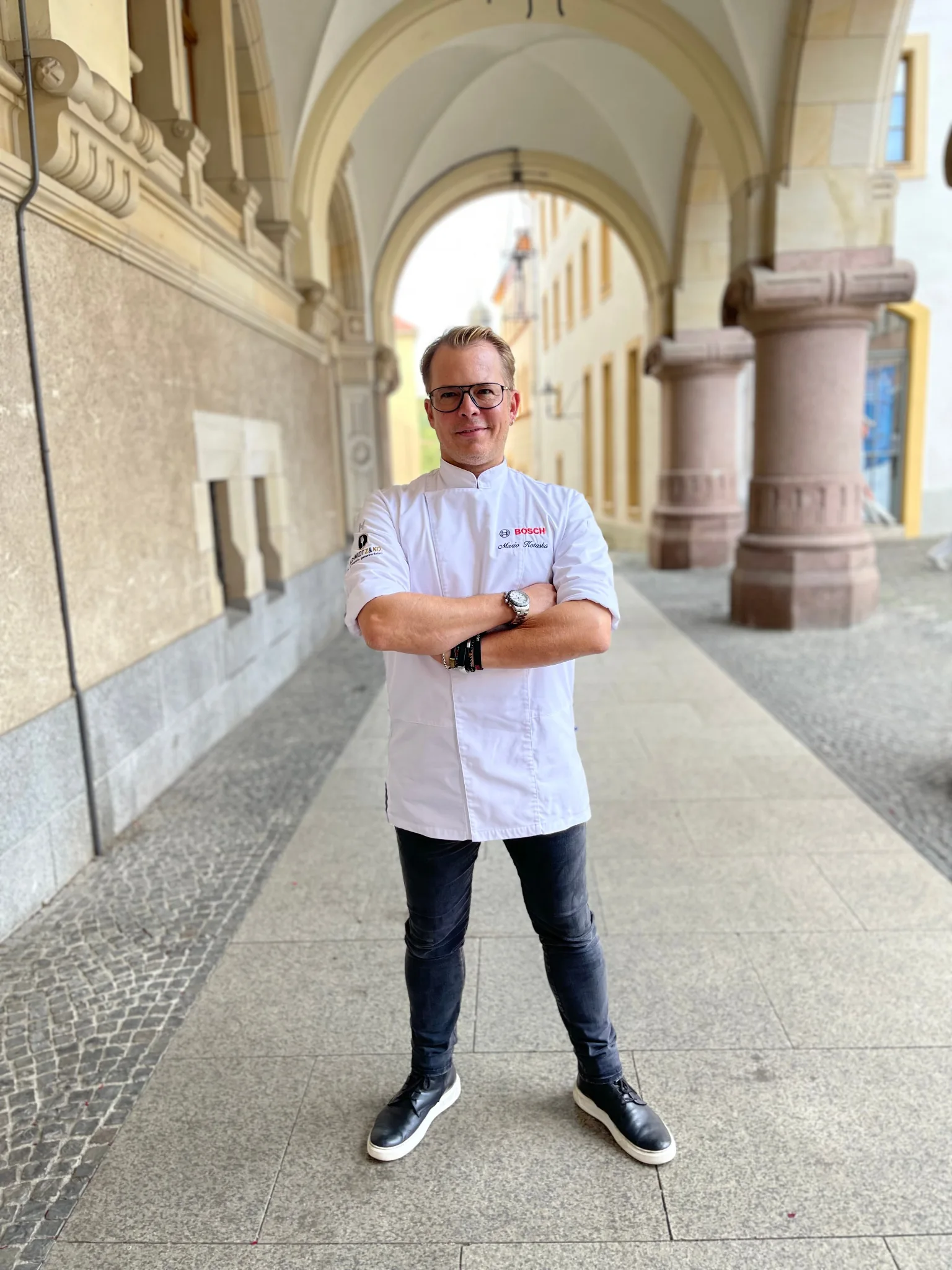 Mario Kotaska in Kochjacke mit verschränkten Armen unter einem Torbogen